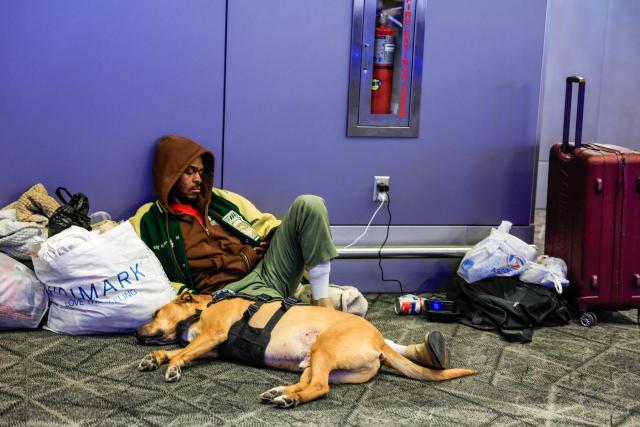 A man rests next to his dog on a lounge of La Guardia Airport on December 23, 2025 in New York. (Photo by kena betancur / AFP)