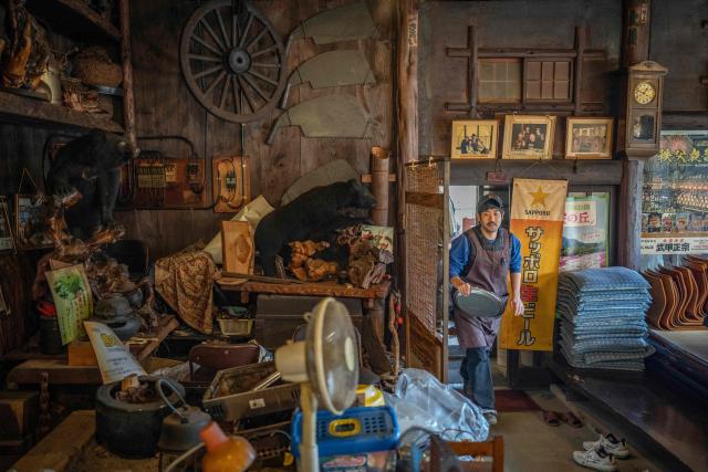 This picture taken on December 12, 2025 shows a member of staff (R) working as taxidermy of bears are displayed at a restaurant which offers bear meat in Chichibu, Saitama prefecture. Since Japan recorded a spike in deadly bear attacks, Koji Suzuki has struggled to keep up with booming demand for grilled cuts of the animal at his restaurant. Cooked on a stone slate -- or in hot pot with vegetables -- the meat comes from bears culled to curb maulings that have killed a record 13 people this year. (Photo by Yuichi YAMAZAKI / AFP) / To go with 'JAPAN-ENVIRONMENT-BEAR-FOOD' by Kyoko Hasegawa and Hiroshi Hiyama in Sapporo