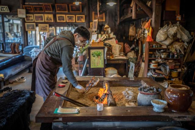 This picture taken on December 12, 2025 shows a member of staff grilling fish over a hearth at a restaurant which offers bear meat in Chichibu, Saitama prefecture. Since Japan recorded a spike in deadly bear attacks, Koji Suzuki has struggled to keep up with booming demand for grilled cuts of the animal at his restaurant. Cooked on a stone slate -- or in hot pot with vegetables -- the meat comes from bears culled to curb maulings that have killed a record 13 people this year. (Photo by Yuichi YAMAZAKI / AFP) / To go with 'JAPAN-ENVIRONMENT-BEAR-FOOD' by Kyoko Hasegawa and Hiroshi Hiyama in Sapporo