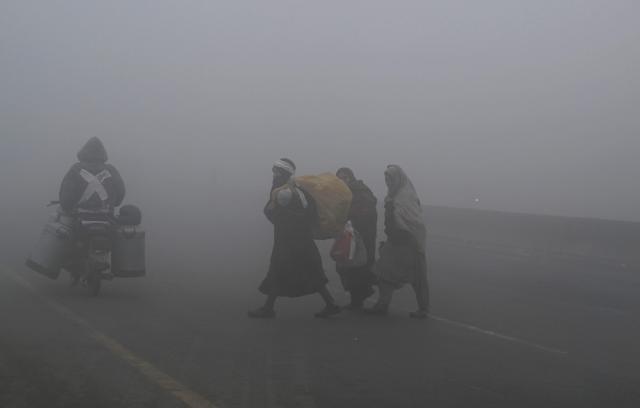 Commuters make their way along a street engulfed in dense smog in Lahore on December 23, 2025. (Photo by Arif ALI / AFP)
