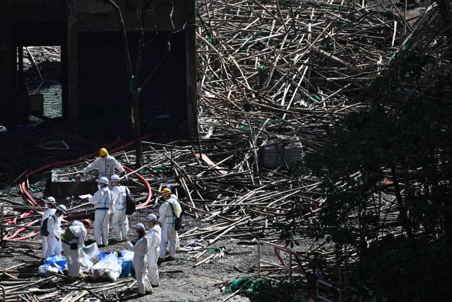 (FILES) Police officers from the Disaster Victim Identification Unit (DVIU), dressed in white-coloured full-body protective gear, enter one of the housing blocks of Wang Fuk Court in the aftermath of the deadly November 26 fire, in Hong Kong on November 29, 2025. Thousands are grieving the 161 killed at Wang Fuk Court, a disaster few could imagine happening in one of Asia's safest and most developed cities. Even as the Hong Kong government forges ahead with investigations and relief efforts, experts caution that the psychological scars will be hard to heal for survivors, bereaved families and onlookers alike. (Photo by Philip FONG / AFP)