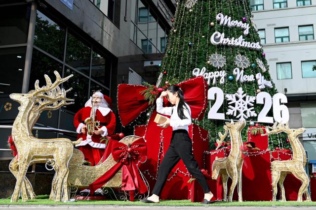 A woman walks past Christmas decorations outside a building in Hanoi on December 24, 2025. (Photo by Nhac NGUYEN / AFP)