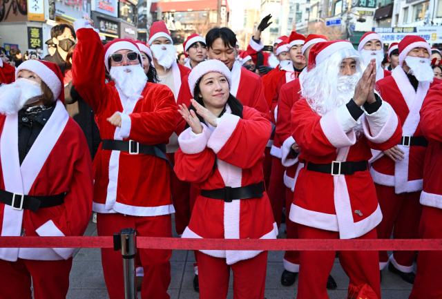 South Korean volunteers in Santa Claus outfits dance during a launch ceremony before delivering gifts to some 800 underprivileged children on Christmas Eve, in Seoul on December 24, 2025. (Photo by Jung Yeon-je / AFP)