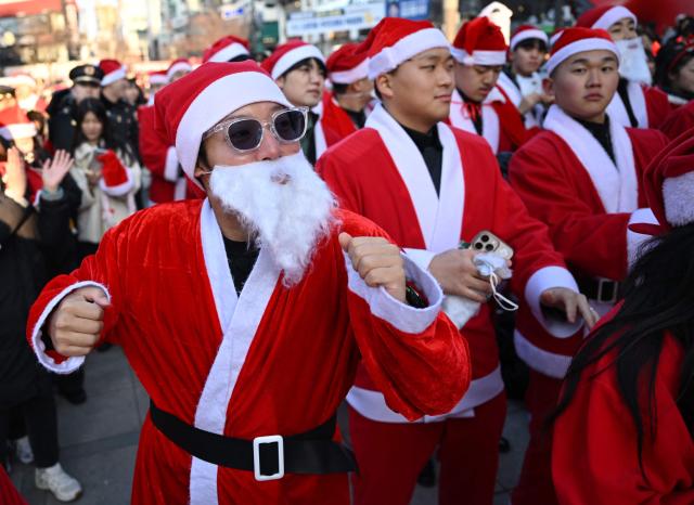 South Korean volunteers in Santa Claus outfits dance during a launch ceremony before delivering gifts to some 800 underprivileged children on Christmas Eve, in Seoul on December 24, 2025. (Photo by Jung Yeon-je / AFP)