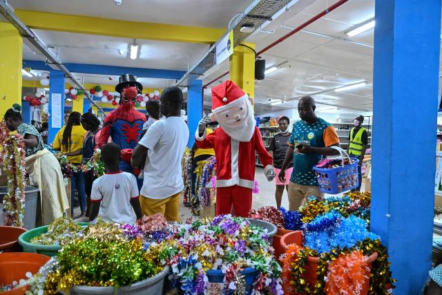 Customers stand near a man dressed as Santa Claus as they buy decoration garlands in a store selling toys and other items for Christmas celebrations in Abidjan on December 23, 2025. (Photo by Sia KAMBOU / AFP)