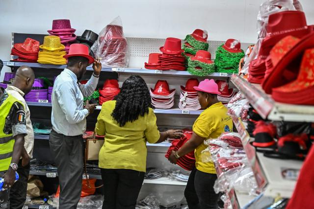 Customers buy Christmas hats in a store selling toys and other decorations for Christmas celebrations in Abidjan on December 23, 2025. (Photo by Sia KAMBOU / AFP)
