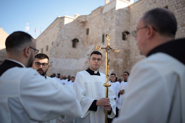 Clergymen and alter boys wait ahead of Christmas service in the Manger Square outside the Church of the Nativity (R) in the biblical city of Bethlehem in the occupied West Bank on Christmas eve on December 24, 2025. Scouts marched under a clear blue sky in Bethlehem on December 24, 2025, as the Palestinian city emerged from the shadow of the war in Gaza to celebrate its first festive Christmas in more than two years. Throughout the Gaza war that began with Hamas's attack on Israel in October 2023, a sombre tone marked Chistmases in Bethlehem, the biblical birthplace of Jesus Christ. (Photo by ilia yefimovich / AFP)