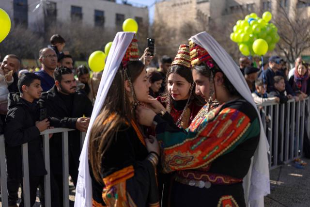 Women in traditional Palestinian dress adjust their costumes before posing for a photograph in front of the Christmas tree in Nativity Square, as people gather ahead of the arrival of Latin Patriarch of Jerusalem to celebrate Christmas Mass, in the biblical city of Bethlehem in the Israeli-occupied West Bank on Christmas eve on December 24, 2025. Scouts marched under a clear blue sky in Bethlehem on December 24, 2025, as the Palestinian city emerged from the shadow of the war in Gaza to celebrate its first festive Christmas in more than two years. Throughout the Gaza war that began with Hamas's attack on Israel in October 2023, a sombre tone marked Chistmases in Bethlehem, the biblical birthplace of Jesus Christ. (Photo by ILIA YEFIMOVICH / AFP)