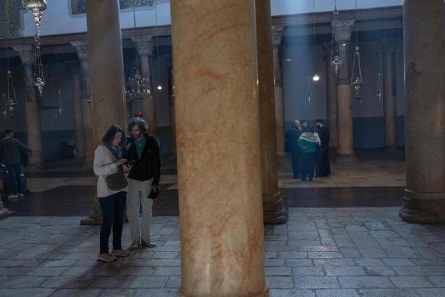 People stand in the Church of the Navtivity ahead of the arrival of Latin Patriarch of Jerusalem to celebrate Christmas Mass, in the biblical city of Bethlehem in the Israeli-occupied West Bank on Christmas eve on December 24, 2025. Scouts marched under a clear blue sky in Bethlehem on December 24, 2025, as the Palestinian city emerged from the shadow of the war in Gaza to celebrate its first festive Christmas in more than two years. Throughout the Gaza war that began with Hamas's attack on Israel in October 2023, a sombre tone marked Chistmases in Bethlehem, the biblical birthplace of Jesus Christ. (Photo by ILIA YEFIMOVICH / AFP)