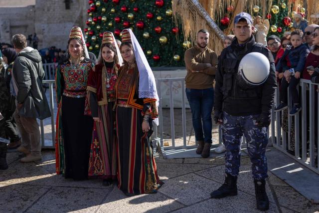 Women in traditional Palestinian dress pose in front of the Christmas tree in Nativity Square as people gather celebrating ahead of the arrival of Latin Patriarch of Jerusalem for the Christmas Service in the biblical city of Bethlehem in the Israeli-occupied West Bank on Christmas eve on December 24, 2025. Scouts marched under a clear blue sky in Bethlehem on December 24, 2025, as the Palestinian city emerged from the shadow of the war in Gaza to celebrate its first festive Christmas in more than two years. Throughout the Gaza war that began with Hamas's attack on Israel in October 2023, a sombre tone marked Chistmases in Bethlehem, the biblical birthplace of Jesus Christ. (Photo by ILIA YEFIMOVICH / AFP)