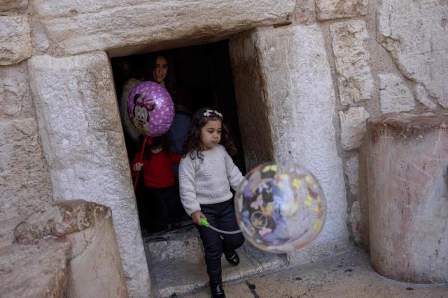 Children holding balloons walks through the Door of Humility in the Chruch of the Nativity as people gather for Christmas eve celebrations in the biblical West Bank city of Bethlehem, believed to be the birthplace of Jesus Christ, on December 24, 2025. Scouts marched under a clear blue sky in Bethlehem on December 24, 2025, as the Palestinian city emerged from the shadow of the war in Gaza to celebrate its first festive Christmas in more than two years. Throughout the Gaza war that began with Hamas's attack on Israel in October 2023, a sombre tone marked Chistmases in Bethlehem, the biblical birthplace of Jesus Christ. (Photo by ILIA YEFIMOVICH / AFP)