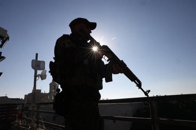 A Palestinian security officer stands guard as pilgrims, tourists and Palestinians wait for the arrival of the Latin Patriarch of Jerusalem to lead the Christmas Mass in the Church of the Nativity in the Israeli-occupied West Bank city of Bethlehem, believed to be the birthplace of Jesus Christ, on December 24, 2025. Palestinian Scouts marched under a clear blue sky in Bethlehem on December 24, 2025, as the Palestinian city emerged from the shadow of the war in Gaza to celebrate its first festive Christmas in more than two years. Throughout the Gaza war that began with Hamas's attack on Israel in October 2023, a sombre tone marked Chistmases in Bethlehem, the biblical birthplace of Jesus Christ. (Photo by HAZEM BADER / AFP)