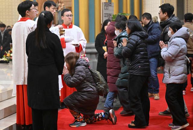 Catholic devotees wait in a queue to receive Holy Communion from a priest during the Christmas Eve mass at the Xishiku Church in Beijing on December 24, 2025. (Photo by Adek BERRY / AFP)
