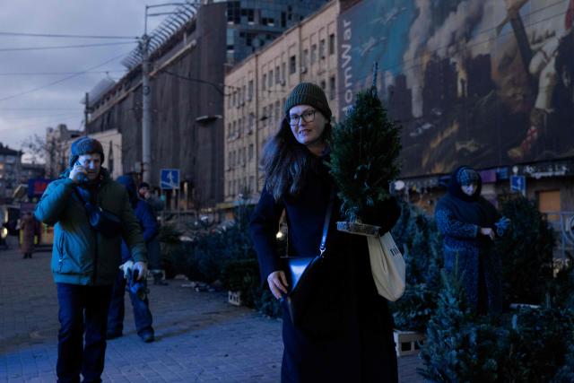 A woman carries a small Fir Tree better known as a Christmas tree at a street market near damaged buildings in Kyiv on Christmas Eve celebrations on December 24, 2025, amid the Russian invasion of Ukraine. (Photo by Tetiana DZHAFAROVA / AFP)