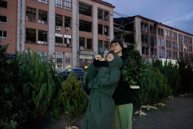 A couple poses with a Fir Tree better known as a Christmas tree at a street market near damaged buildings in Kyiv on Christmas Eve celebrations on December 24, 2025, amid the Russian invasion of Ukraine. (Photo by Tetiana DZHAFAROVA / AFP)
