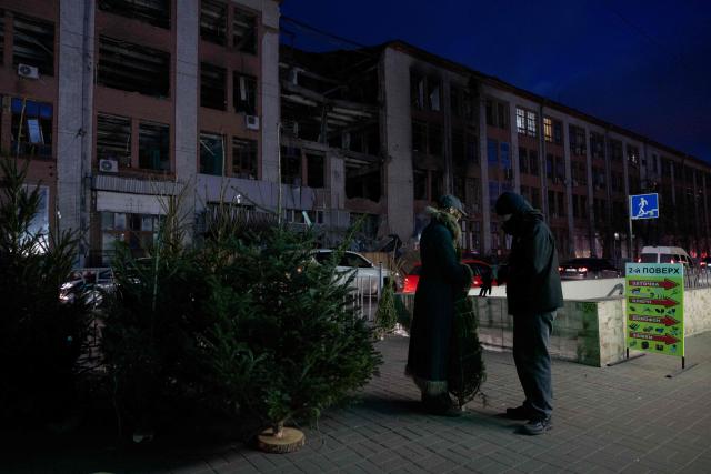 A woman holds a Fir Tree better known as a Christmas tree at a street market near damaged buildings in Kyiv on Christmas Eve celebrations on December 24, 2025, amid the Russian invasion of Ukraine. (Photo by Tetiana DZHAFAROVA / AFP)