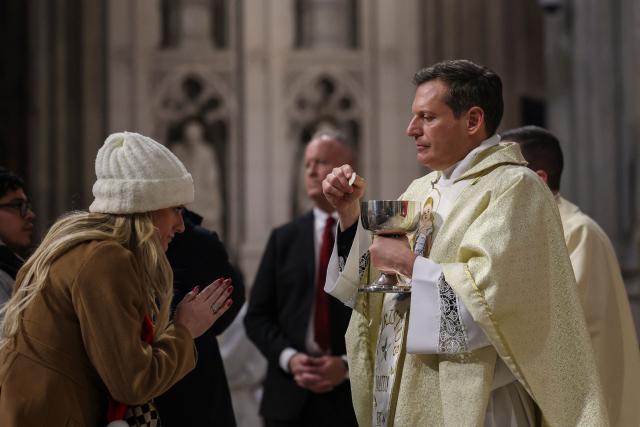 A person receives communion during Christmas Mass at St. Patrick’s Cathedral on Christmas Eve on December 24, 2025 in New York. (Photo by ANGELA WEISS / AFP)