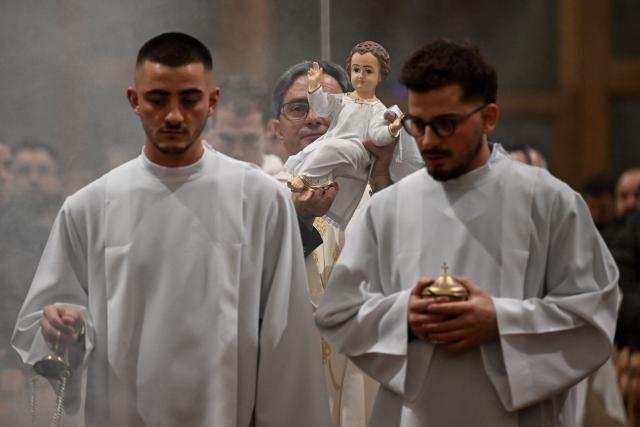 A priest holds a statue of Baby Jesus as worshippers attend Christmas Eve mass at the Mother Teresa Cathedral in Pristina on December 25, 2025. (Photo by Armend NIMANI / AFP)
