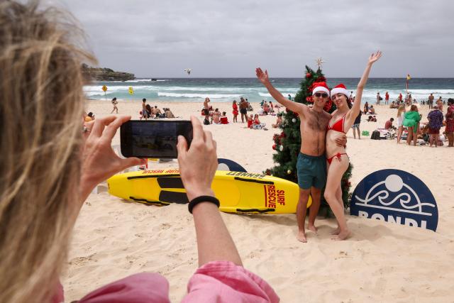 Tourists wearing Christmas costumes pose in front of a Christmas tree on the sand at Bondi Beach in Sydney on December 25, 2025. (Photo by DAVID GRAY / AFP)