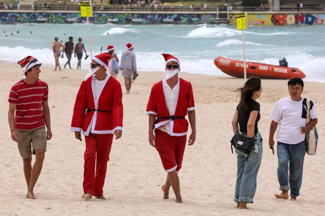 Tourists wearing Christmas costumes walk along the sand of Bondi Beach in Sydney on December 25, 2025. (Photo by DAVID GRAY / AFP)