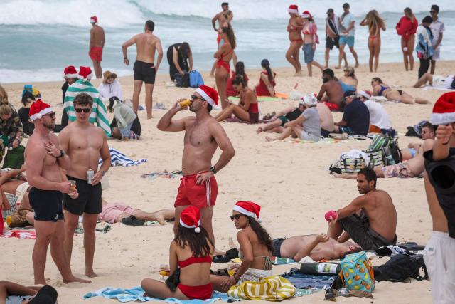 Tourists wearing Christmas hats are seen on the sand of Bondi Beach in Sydney on December 25, 2025. (Photo by DAVID GRAY / AFP)