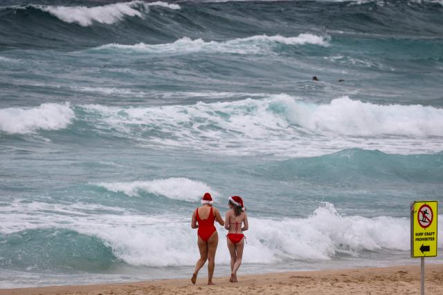 Tourists wearing Christmas hats walk along the sand at Bondi Beach on Christmas Day in Sydney on December 25, 2025. (Photo by DAVID GRAY / AFP)