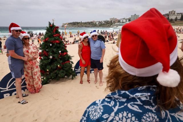 Tourists wearing Christmas costumes pose in front of a Christmas tree on the sand at Bondi Beach in Sydney on December 25, 2025. (Photo by DAVID GRAY / AFP)