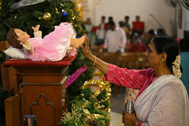 A devotee touches the statue of baby Jesus while praying at the Santhome Cathedral Basilica church on the occasion of Christmas, in Chennai on December 25, 2025. (Photo by R.Satish BABU / AFP)