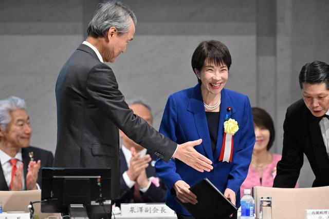 Japan's Prime Minister Sanae Takaichi (C) is greeted by Yoshinobu Tsutsui, Chairman of the Japan Business Federation, or Keidanren, upon her arrival at the 14th Keidanren Council Meeting in Tokyo on December 25, 2025. (Photo by Kazuhiro NOGI / AFP)