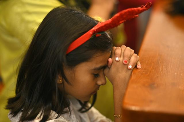 A girl prays during a Christmas mass at a church in Bengaluru on December 25, 2025. (Photo by Idrees MOHAMMED / AFP)