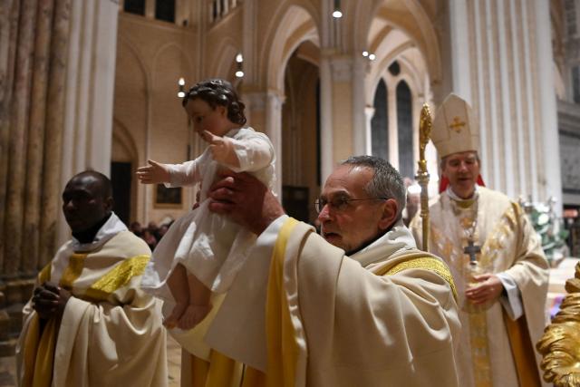 French rector of the cathedral Emmanuel Blondeau (C) presents a figure of Baby Jesus next to French bishop of Chartres Monsignor Philippe Christory (R) after celebrating the midnight Christmas mass at Cathedral of Our Lady of Chartres in Chartres, north-central France in the early hours of December 25, 2025. (Photo by JEAN-FRANCOIS MONIER / AFP)