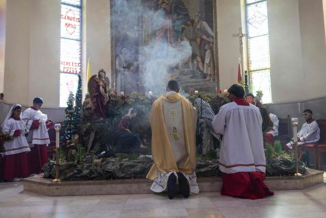 Abouna Bashar Basiel and Alter servers gather around a manger scene in which Joseph wears a Palestinian keffiyeh, during a Christmas morning mass at the Christ the Redeemer Church in the mostly Christian town of Taybeh, in the Israeli-occupied West Bank on December 25, 2025. (Photo by ILIA YEFIMOVICH / AFP)