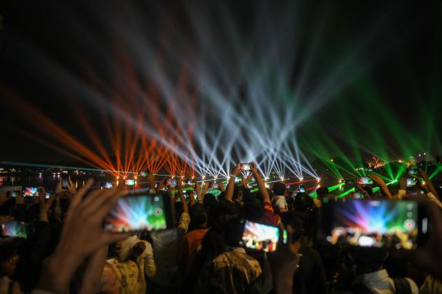 People use their mobile phones to capture a laser show during the inauguration of the Kankaria Carnival in Ahmedabad on December 25, 2025. (Photo by Shammi MEHRA / AFP)