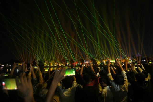 People use their mobile phones to capture a laser show during the inauguration of the Kankaria Carnival in Ahmedabad on December 25, 2025. (Photo by Shammi MEHRA / AFP)