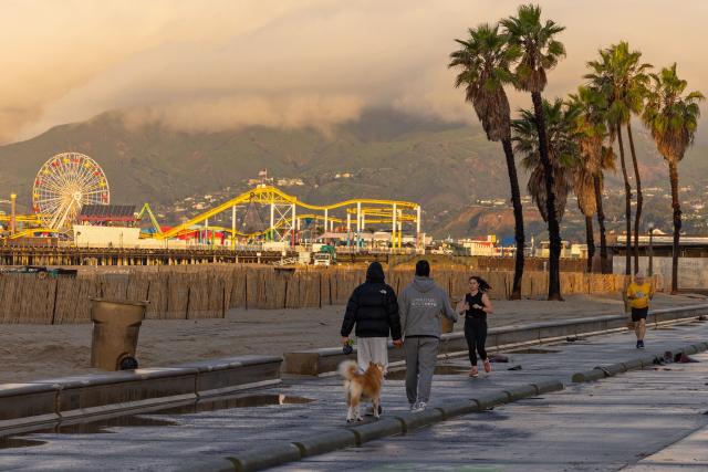 People walk on a bike path during a break from the rain storms impacting Southern California on December 25, 2025 in Santa Monica, California. Torrential rains unleashed flash floods and warnings of debris flow across southern California, particularly in fire-scarred areas, with further downpours forecast for Thursday as authorities declared a state of emergency in several counties. Driven by an atmospheric river known as "the Pineapple Express," which moves heavy moisture from the tropical climes of Hawaii to the US West Coast, the storm was expected to deliver months' worth of rain over a few days. (Photo by Robyn Beck / AFP)