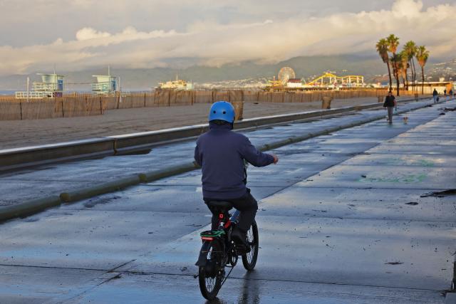 CORRECTION / A bicycle rider heads towards the Santa Monica pier during a break from the rain storms impacting Southern California on December 25, 2025 in Santa Monica, California. Torrential rains unleashed flash floods and warnings of debris flow across southern California, particularly in fire-scarred areas, with further downpours forecast for Thursday as authorities declared a state of emergency in several counties. Driven by an atmospheric river known as "the Pineapple Express," which moves heavy moisture from the tropical climes of Hawaii to the US West Coast, the storm was expected to deliver months' worth of rain over a few days. (Photo by Jonathan ALCORN / AFP) / The erroneous mention[s] appearing in the metadata of this photo by Robyn Beck has been modified in AFP systems in the following manner: [Jonathan Alcorn] instead of [Robyn Beck]. Please immediately remove the erroneous mention[s] from all your online services and delete it (them) from your servers. If you have been authorized by AFP to distribute it (them) to third parties, please ensure that the same actions are carried out by them. Failure to promptly comply with these instructions will entail liability on your part for any continued or post notification usage. Therefore we thank you very much for all your attention and prompt action. We are sorry for the inconvenience this notification may cause and remain at your disposal for any further information you may require.