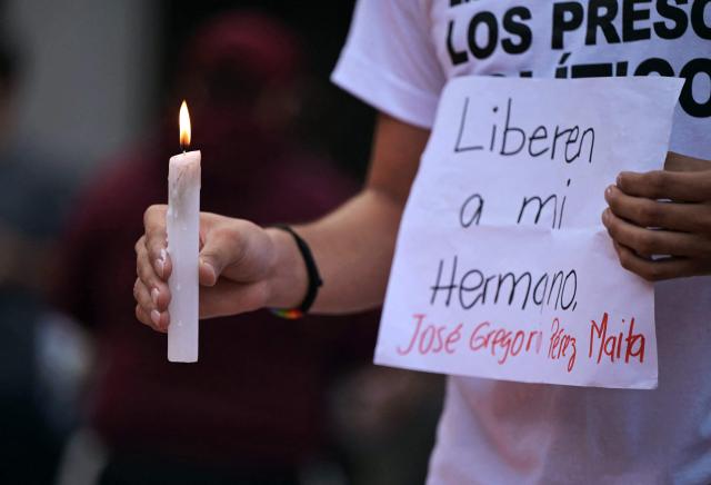 (FILES) A man holds a candle and a sign asking for the release of his brother, during a vigil called by the opposition demanding freedom for political prisoners arrested during protest following the contested re-election of Venezuelan President Nicolas Maduro in Caracas, August 8, 2024. At least 60 post-election detainees were released from prison on December 25, 2025, a non-governmental organisation made up of human rights activists and relatives of political prisoners reported. Those released had been arrested amid the political crisis triggered by President Nicolas Maduro's re-election in July 2024 for a third term amid allegations of fraud from the opposition. (Photo by Yuri CORTEZ / AFP)