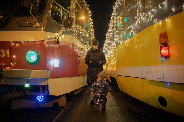 A woman with a child walks in between trams decorated with garlands on Christmas Day in Kharkiv on December 25, 2025, amid the Russian invasion of Ukraine. (Photo by Ivan SAMOILOV / AFP)