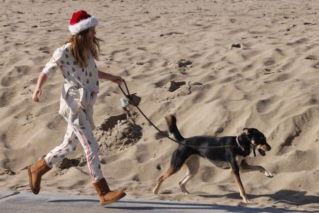 A woman runs with her dog during a break in the rain storms affecting Southern California on December 25, 2025 in Venice, California. Torrential rains unleashed flash floods and warnings of debris flow across southern California, particularly in fire-scarred areas, with further downpours forecast for Thursday as authorities declared a state of emergency in several counties. Driven by an atmospheric river known as "the Pineapple Express," which moves heavy moisture from the tropical climes of Hawaii to the US West Coast, the storm was expected to deliver months' worth of rain over a few days. (Photo by Jonathan Alcorn / AFP)