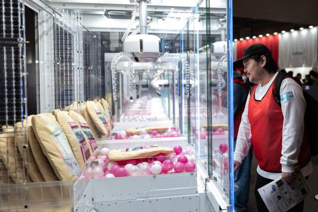 This picture taken on November 14, 2025 shows people gathering in front of claw crane game machines displayed at the booth of Japanese video game and entertainment company Sega, during the Amusement Expo 2025 in Tokyo. As school and work wraps up, crowds gradually fill Tokyo's many bustling arcade halls —- not to battle it out in fighting games, but to snag plush toys from claw machines. (Photo by Philip FONG / AFP) / To go with 'JAPAN-ANIMATION-GAME-ARCADE, FOCUS' by Mathias Cena