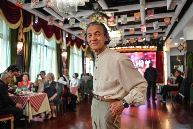 This photo taken on December 10, 2025 shows an elderly man posing for a picture at the Hai Shang Jiu Meng Dance Hall in the Changning district of Shanghai. It was just a regular Wednesday at a lunchtime dance club in Shanghai, where dance hall culture has been deeply rooted in the city's identity since its jazz-age heyday. On any given day, multiple venues host hours-long daytime sessions across the finance hub, some starting as early as 6 am. Establishments like the historic Paramount Ballroom are time capsules from the 1930s, while others flash with neon pink and green rave lights in the early afternoon. (Photo by Hector RETAMAL / AFP) / To go with 'CHINA-LIFESTYLE-DANCE-HISTORY-DEMOGRAPHICS, REPORTAGE' by Rita QIAN