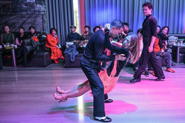 This photo taken on December 10, 2025 shows Xu Li (R), 60, dancing with a partner at the Shiguang Dance Hall in the Putuo district of Shanghai. It was just a regular Wednesday at a lunchtime dance club in Shanghai, where dance hall culture has been deeply rooted in the city's identity since its jazz-age heyday. On any given day, multiple venues host hours-long daytime sessions across the finance hub, some starting as early as 6 am. Establishments like the historic Paramount Ballroom are time capsules from the 1930s, while others flash with neon pink and green rave lights in the early afternoon. (Photo by Hector RETAMAL / AFP) / To go with 'CHINA-LIFESTYLE-DANCE-HISTORY-DEMOGRAPHICS, REPORTAGE' by Rita QIAN