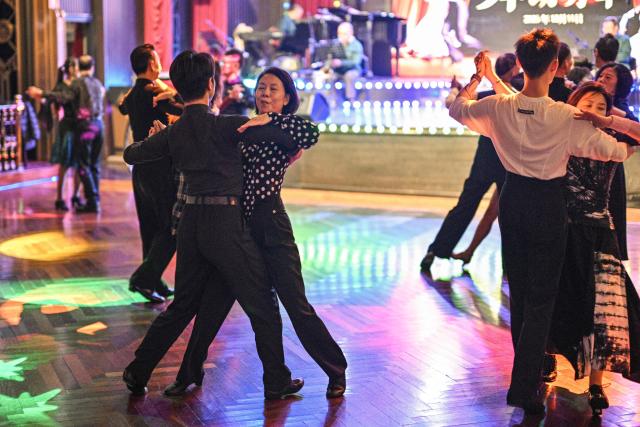 This photo taken on December 11, 2025 shows Kuai Yuqin (C), dancing with a partner at the Paramount Ballroom in the Jing'An district of Shanghai. It was just a regular Wednesday at a lunchtime dance club in Shanghai, where dance hall culture has been deeply rooted in the city's identity since its jazz-age heyday. On any given day, multiple venues host hours-long daytime sessions across the finance hub, some starting as early as 6 am. Establishments like the historic Paramount Ballroom are time capsules from the 1930s, while others flash with neon pink and green rave lights in the early afternoon. (Photo by Hector RETAMAL / AFP) / To go with 'CHINA-LIFESTYLE-DANCE-HISTORY-DEMOGRAPHICS, REPORTAGE' by Rita QIAN