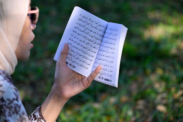 A woman reads copy of the Koran as she prays for relatives who lost their lives in the 2004 Indian Ocean tsunami at a mass grave in Siron, Aceh province on December 26, 2025. On December 26, 2004, a magnitude 9.1 earthquake struck the coast of Sumatra in Indonesia and triggered a huge tsunami across the Indian Ocean that killed more than 220,000 people in a dozen countries. (Photo by CHAIDEER MAHYUDDIN / AFP)