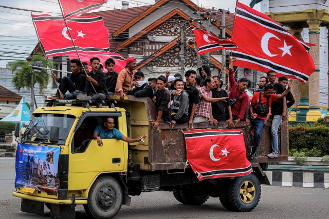 People hold Free Aceh Movement (GAM) flags while escorting humanitarian aid, meant for survivors of the recent devastating floods in Sumatra, in Bireuen, Aceh Province on December 25, 2025. Despite the efforts by the Indonesian government, frustration is mounting over sluggish relief efforts which has fuelled demands on Jakarta to declare a national disaster and permit international assistance into affected areas. The provincial government in Aceh said it had already turned to several United Nations agencies for help, citing their previous aid campaigns in the wake of the 2004 tsunami. (Photo by AMANDA JUFRIAN / AFP)
