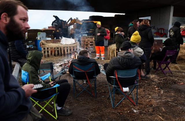 Protesters gather around a fire before leaving the A63 highway in Cestas south-western France, on December 26, 2025 during a farmers demonstration to protest against the government's mandatory culling protocol for cattle herds affected by lumpy skin disease (dermatose nodulaire contagieuse).  (Photo by ROMAIN PERROCHEAU / AFP)