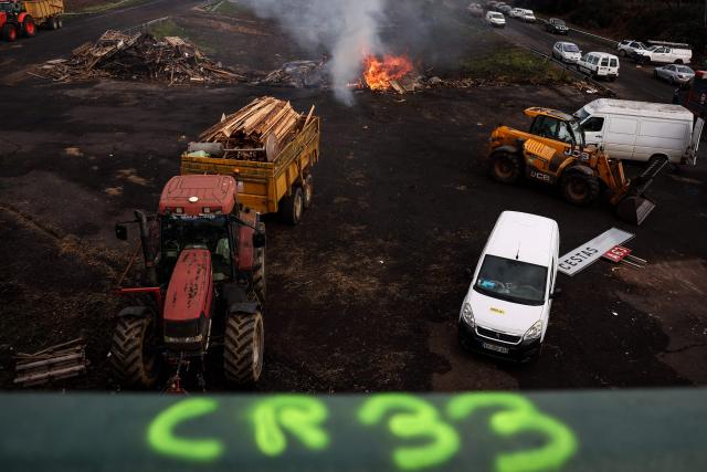 A photograph taken on December 26, 2025 shows wood and hay set on fire and tractors blocking the A63 highway in Cestas south-western France, during a farmers demonstration to protest against the government's mandatory culling protocol for cattle herds affected by lumpy skin disease (dermatose nodulaire contagieuse).  (Photo by ROMAIN PERROCHEAU / AFP)