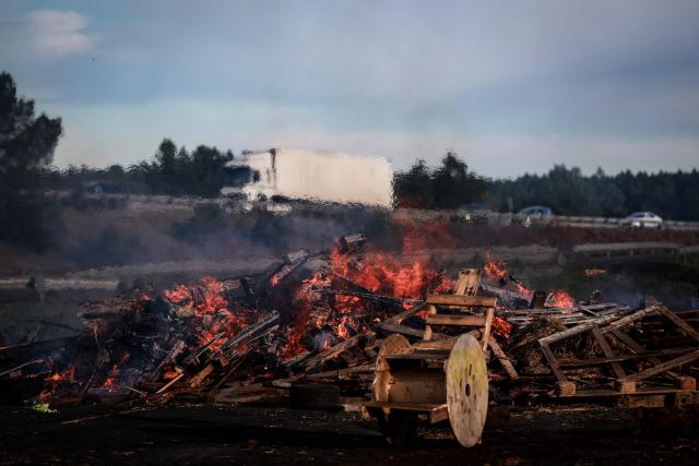 A photograph taken on December 26, 2025 shows wood and hay set on fire and tractors blocking the A63 highway in Cestas south-western France, during a farmers demonstration to protest against the government's mandatory culling protocol for cattle herds affected by lumpy skin disease (dermatose nodulaire contagieuse).  (Photo by ROMAIN PERROCHEAU / AFP)