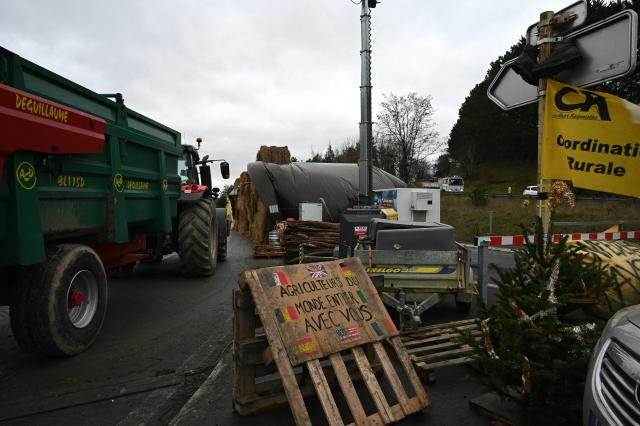 Farmers from the 'Coordination Rurale' (CR32) union display a placard which reads "Farmers from all over the world are with you" as they block a roundabout as they protest against the French government's mandatory culling protocol for cattle herds affected by lumpy skin disease (dermatose nodulaire contagieuse), in Auch, southwestern France, on December 26, 2025. (Photo by Matthieu RONDEL / AFP)