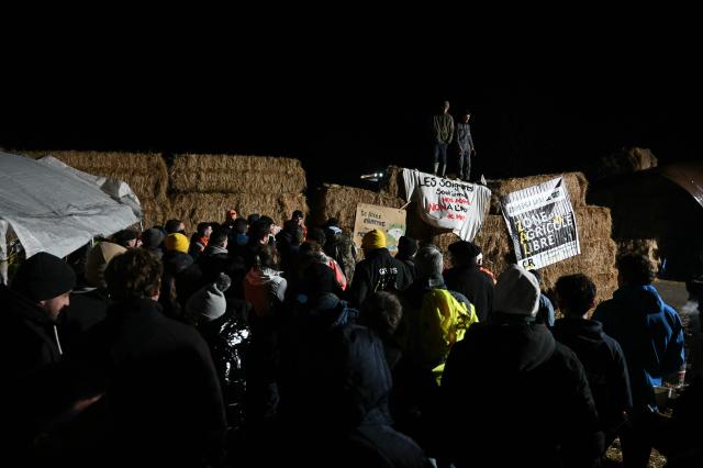 Farmers of "Coordination Rurale" (CR32) agricultural union gather for a speeches from members standing atop bales of hay as they block a roundabout in protest against the French government's mandatory culling protocol for cattle herds affected by lumpy skin disease (dermatose nodulaire contagieuse), in Auch, southwestern France, on December 26, 2025. (Photo by Matthieu RONDEL / AFP)